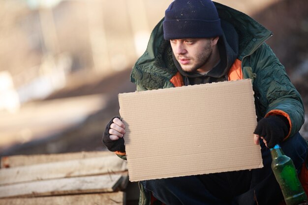 Un sans-abri tient un carton vierge pour votre texte