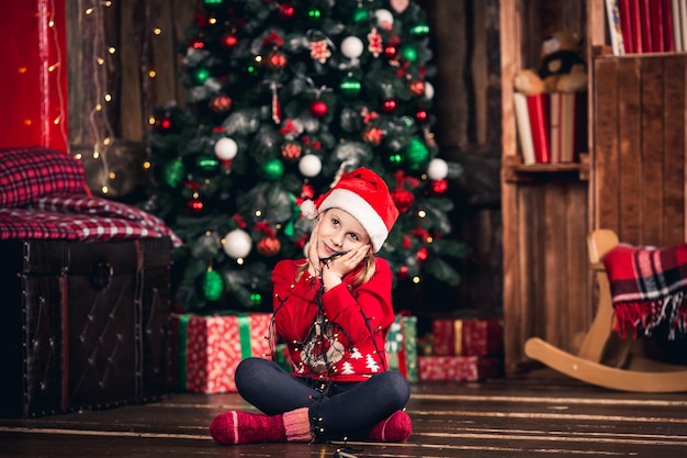 Santa girl enveloppé dans une guirlande assis sur le sol