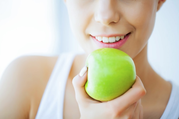 Santé et beauté, belle jeune fille aux dents blanches tenant les mains de pomme verte fraîche