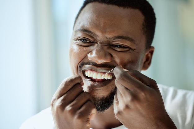 Santé beauté et dents d'un homme noir avec du fil dentaire pour la routine d'hygiène bucco-dentaire du matin avec accent Soins dentaires soins personnels et bien-être de la personne nettoyant et vérifiant les dents dans le miroir de la salle de bain