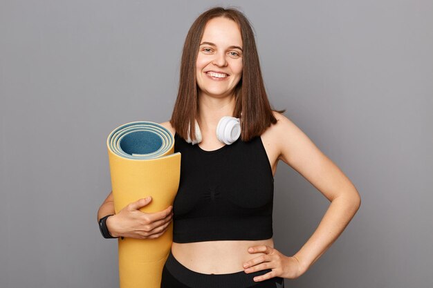 La santé est la richesse La forme physique commence par une séance d'entraînement Trouvez l'équilibre grâce au yoga Femme souriante debout portant un tapis de yoga isolé sur fond gris