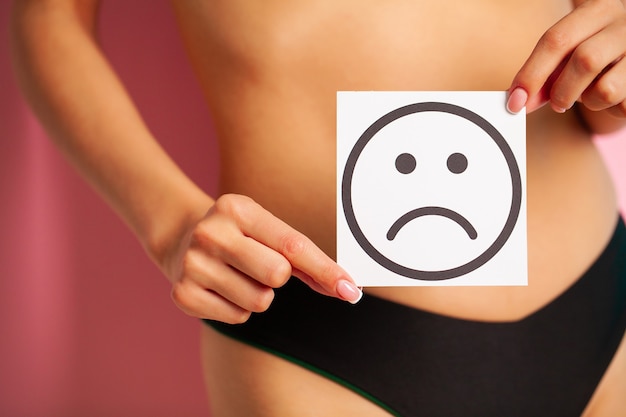 Santé de la femme, corps féminin tenant une carte de sourire triste près de l'estomac.