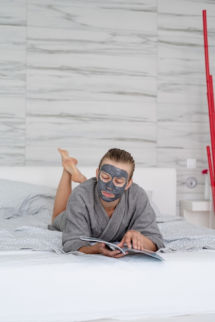 Santé des femmes. Spa et bien-être. Femme avec masque facial relaxant allongé sur le lit en lisant un magazine