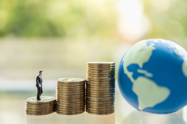 Santé, situation Business et économie Concept. Gens d'affaires miniature homme d'affaires avec masque facial debout et marchant sur une pile de pièces d'or avec mini boule du monde.