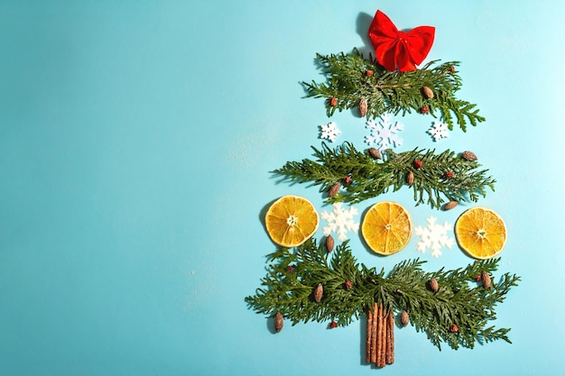 Sapin créatif à partir de branches à feuilles persistantes, de tranches de citron séchées et de flocons de neige. Fond en bois, mise à plat, décor festif, vue de dessus