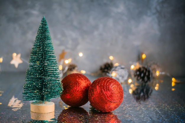 Sapin moelleux décoratif de Noël et deux boules brillantes rouges sur fond gris avec des lumières floues. Fond de Noël. Espace de copie