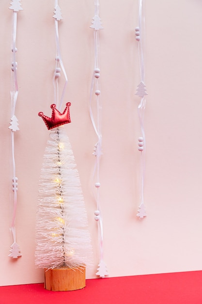 Sapin de Noël blanc avec une couronne rouge sur fond rose clair