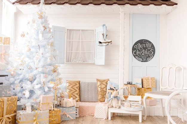 Sapin de Noël blanc décoré de boules de Noël rose doré argenté et de belles boules de verre sur une branche bleue blanche étincelante et féerique, lumières décoratives. Décor de studio photo, maison, fenêtre, porte