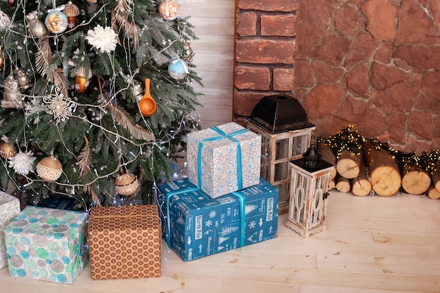 Sapin de Noël avec des cadeaux d'une valeur près d'une cheminée avec une guirlande et du bois de chauffage