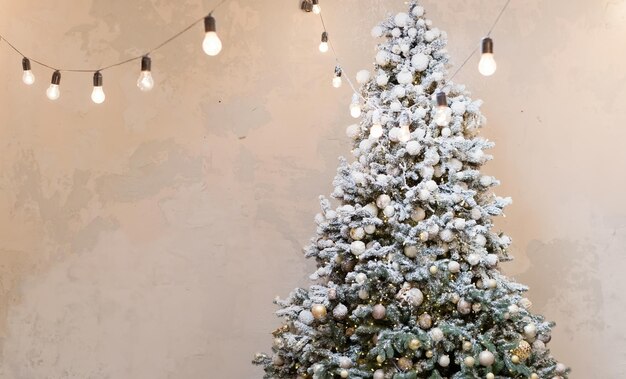Sapin de Noël avec décorations dorées vintage et guirlande lumineuse près du mur lumineux
