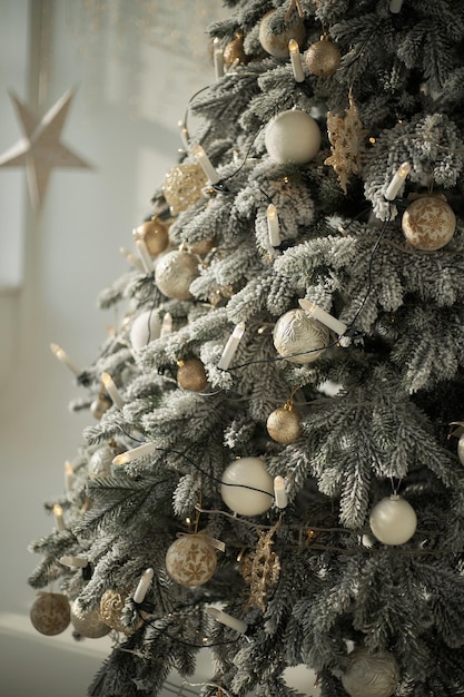 Photo sapin de noël enneigé artificiel luxuriant décoré de boules d'or blanc bougies lumières garland close up in white interior