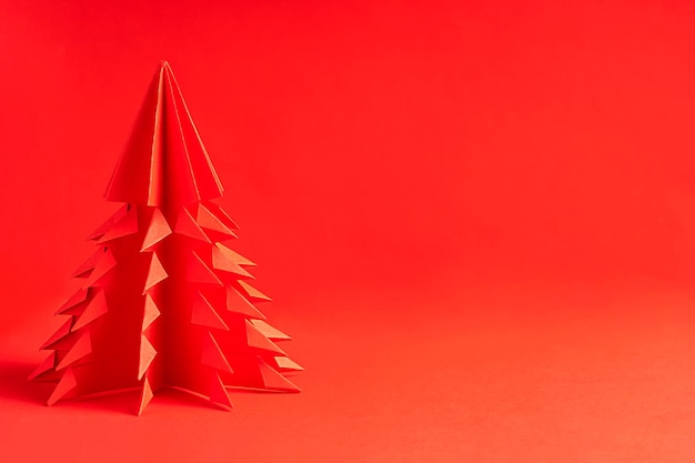 Un sapin de noël fait main en origami en papier kraft plié sur fond rouge vif