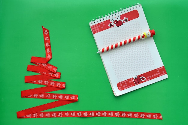 Photo sapin de noël fait de ruban rouge, carnet avec poignée sous la forme d'un bonhomme de neige sur fond vert