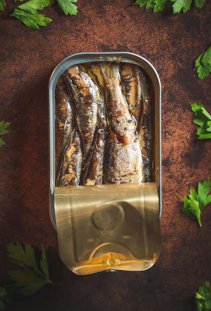 Photo sardines en conserve à l'huile d'olive ouvertes sur une table marron foncé avec du persil