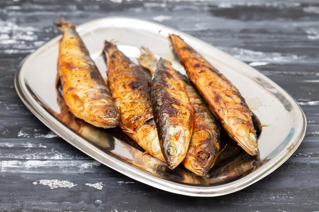 Des sardines grillées dans un plat en métal sur un fond sombre