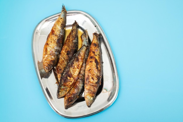 Des sardines grillées dans un plat en métal sur un fond sombre
