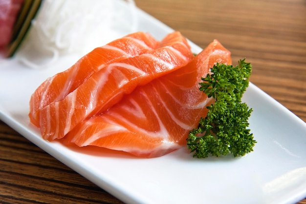 Sashimi de poisson tranché mélangé sur une longue assiette blanche Poisson saumon et sashimi de thon sur fond de bois