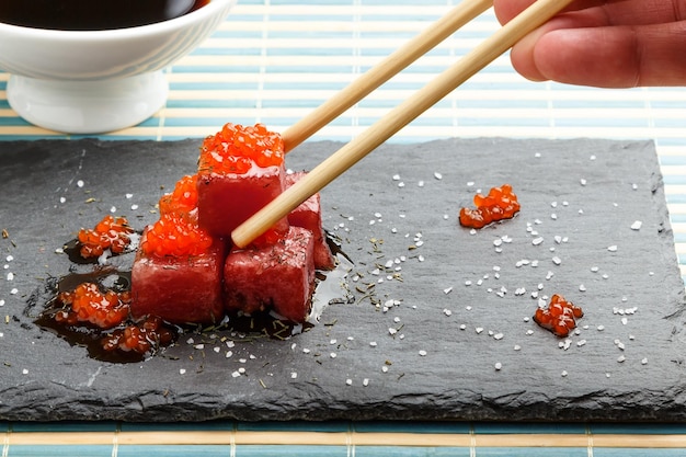 Photo sashimi de thon trempé dans de la sauce soja avec des œufs de saumon, du sel épais et de l'aneth sur de l'ardoise avec des baguettes