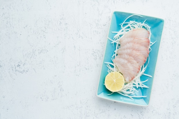 Sashimi de tranches de filet de poisson blanc cru sur une plaque bleue sur blanc