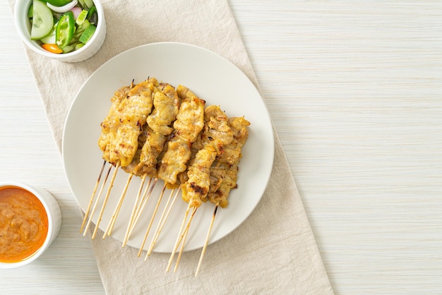 Satay de porc avec cornichons à la sauce aux arachides qui sont des tranches de concombre et des oignons au vinaigre