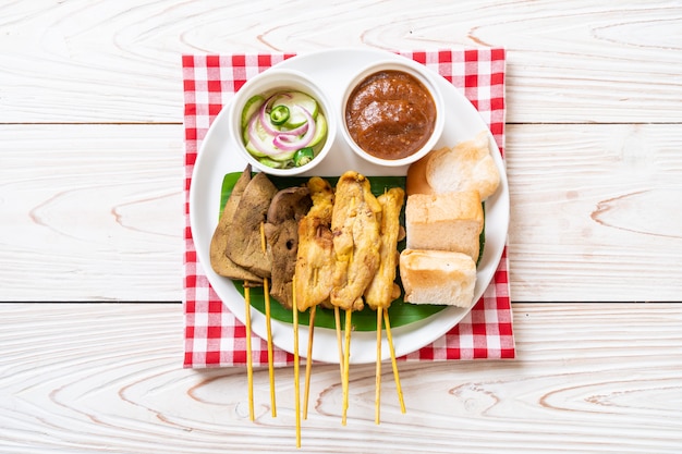 Satay de porc avec votre sauce aux arachides et cornichons qui sont des tranches de concombre et des oignons au vinaigre