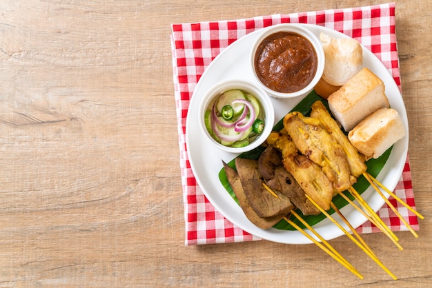 Satay de porc avec votre sauce aux arachides et cornichons qui sont des tranches de concombre et des oignons au vinaigre