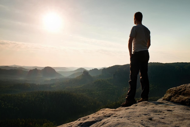 Satisfaire un randonneur en chemise grise et pantalon sombre un homme grand sur le sommet d'une falaise regardant le paysage