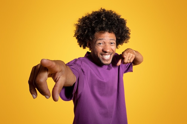 Satisfait excité mec bouclé afro-américain mature en t-shirt violet pointant du doigt la caméra