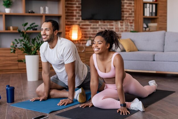 Photo satisfait jeune homme afro-américain et dame en tenue de sport faisant des étirements de jambe et pratiquant le yoga