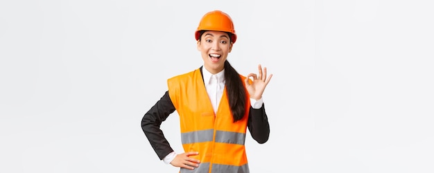 Satisfaite et heureuse femme ingénieure asiatique responsable de la construction dans un casque de sécurité et une veste réfléchissante montrant un geste correct satisfait de garantir la qualité de la construction assure que tout est excellent