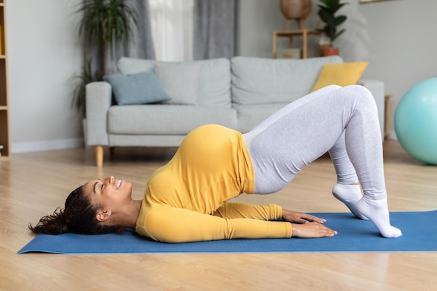 Satisfaite jeune femme enceinte noire avec gros ventre pratiquant le yoga sur tapis profiter de l'entraînement