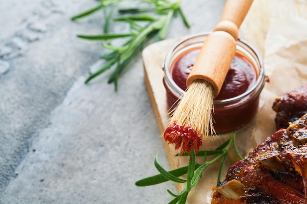 Sauce barbecue chaude et épicée dans un bol en pot avec pinceau à badigeonner sur fond gris pierre ancienne Composition à plat Concept de cuisine américaine Vue de dessus Espace pour le texte