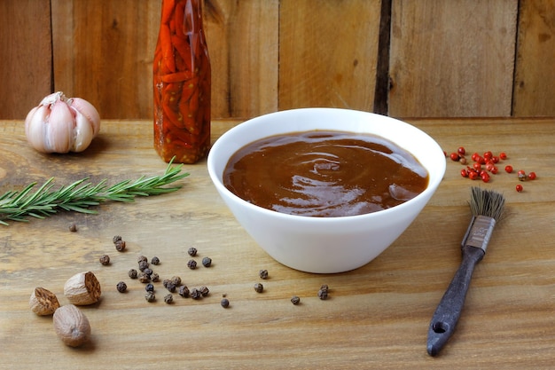 Sauce barbecue dans un bol et pinceau sur des condiments et des herbes de table en bois rustique