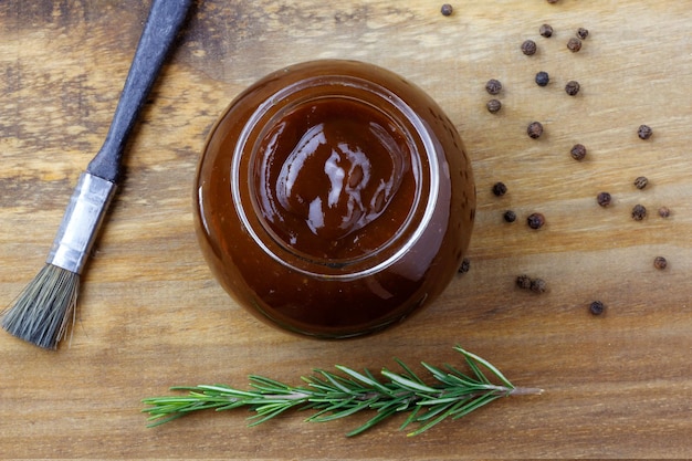 Sauce barbecue dans un bol et pinceau sur des condiments et des herbes de table en bois rustique