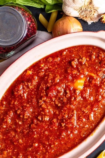 Sauce bolognaise mijoteuse faite maison dans un pot en céramique rouge et penne crue