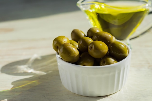 Photo sauce-bot en verre avec de l'huile d'olive vierge extra et des olives vertes fraîches sur une table en bois