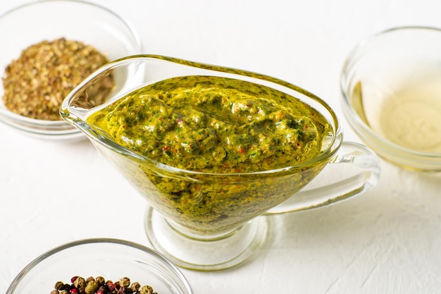 Sauce chimichurri dans un bol de sauce sur fond blanc Diverses épices se trouvent à proximité sauce végétarienne argentine à base d'huile d'olive origan persil