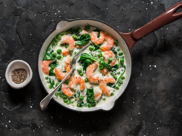 Sauce à la crème d'épinards de crevettes de pois verts frais dans une casserole sur une vue de dessus de fond sombre