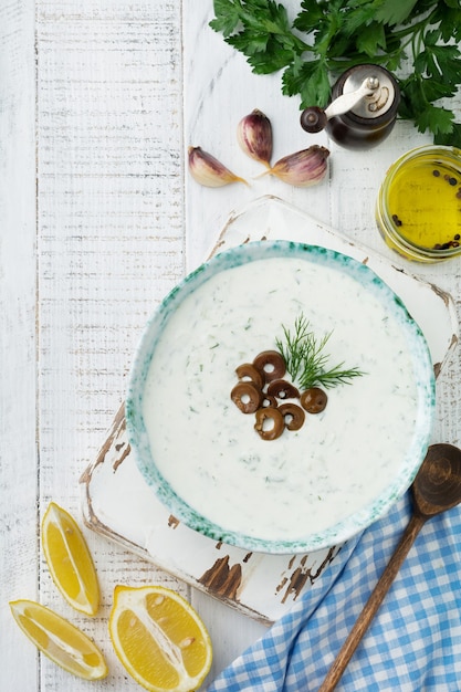 Sauce grecque traditionnelle Tzatziki. Yaourt, concombre, aneth, ail et huile de sel dans un bol en céramique sur une surface en bois clair