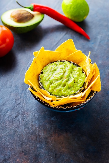 Sauce guacamole avec ingrédients avocat, poivre, citron vert et nachos de maïs sur fond sombre. Guacamole avec ingrédients et chips tortillas nachos. Espace de copie