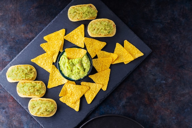 Sauce guacamole mexicaine avec chips de nachos sur une ardoise. Chips tortilla et guacamole sur fond sombre. Espace de copie. Vue de dessus