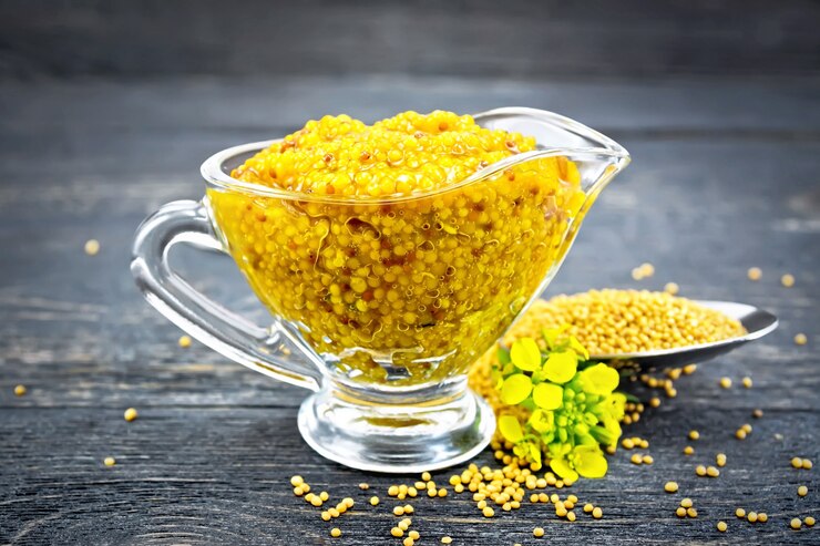 Photo sauce moutarde de dijon dans une saucière en verre, fleurs jaunes et graines de moutarde dans une cuillère sur fond de planche de bois noir