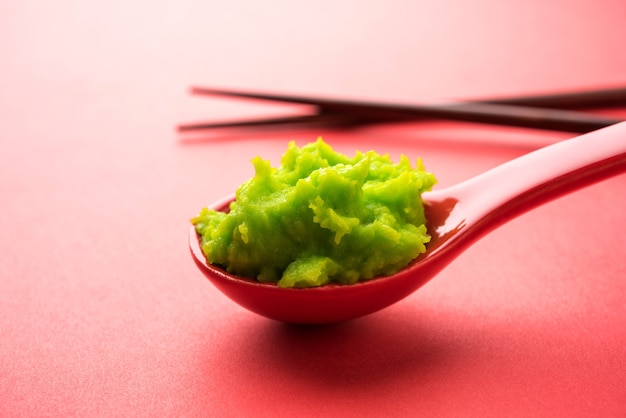 Sauce ou pâte verte au wasabi dans un bol, avec des baguettes ou une cuillère sur un fond coloré uni. mise au point sélective