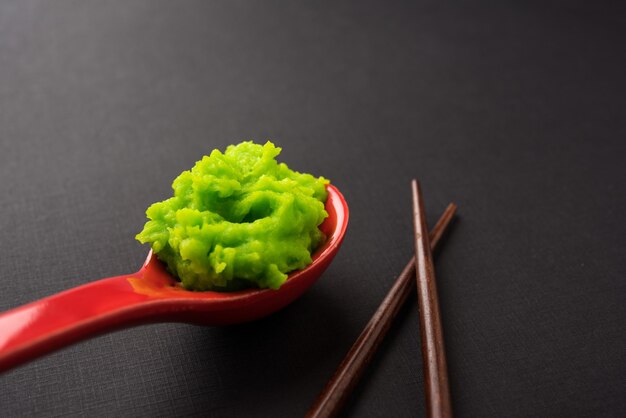 Sauce ou pâte verte au wasabi dans un bol, avec des baguettes ou une cuillère sur un fond coloré uni. mise au point sélective