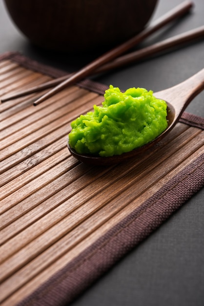 Sauce ou pâte verte au wasabi dans un bol, avec des baguettes ou une cuillère sur un fond coloré uni. mise au point sélective