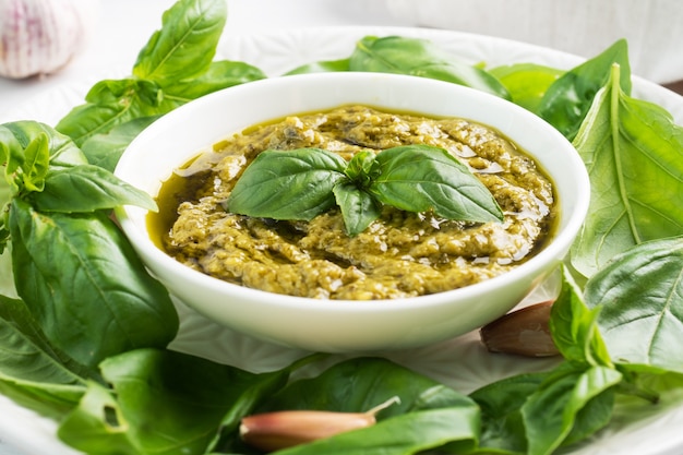 Sauce pesto dans une assiette et feuilles de basilic frais à l'ail.