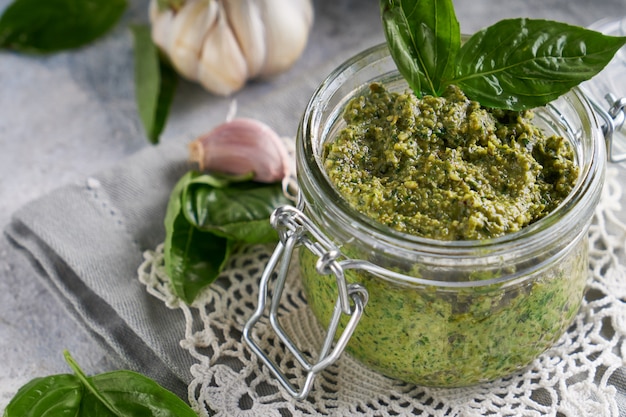 Sauce pesto traditionnelle au basilic italien dans un bocal en verre sur une table en pierre claire