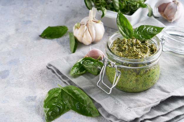 Sauce pesto traditionnelle au basilic italien dans un bocal en verre sur une table en pierre claire