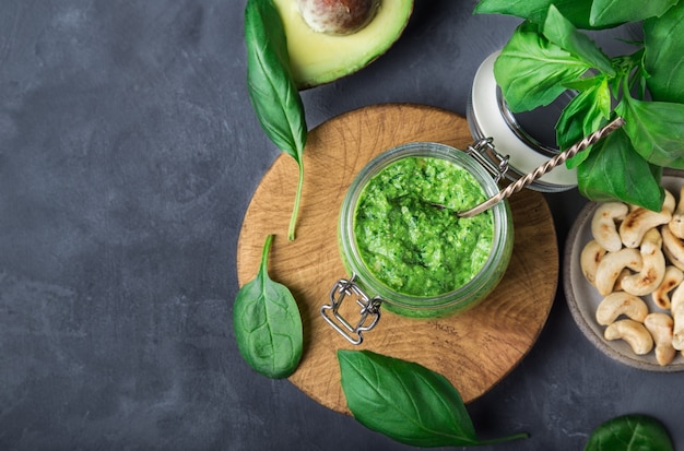 Sauce pesto vegan maison fraîche avec basilic, épinards, noix de cajou et avocat en pot sur béton gris avec des ingrédients