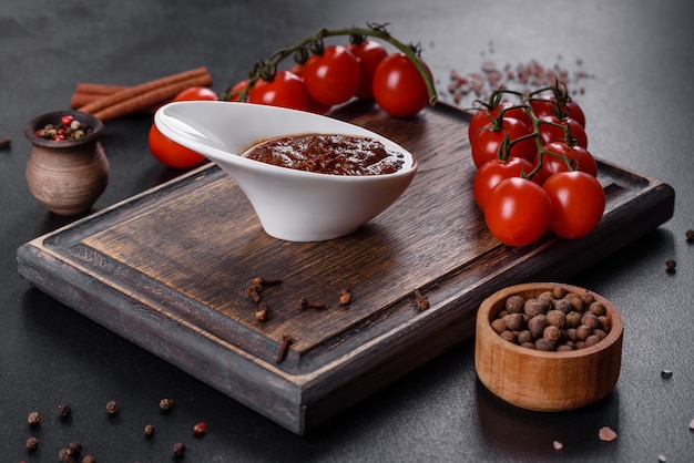 Sauce rouge ou ketchup dans un bol et ingrédients pour la cuisson, épices, ail, tomates et herbes sur fond noir